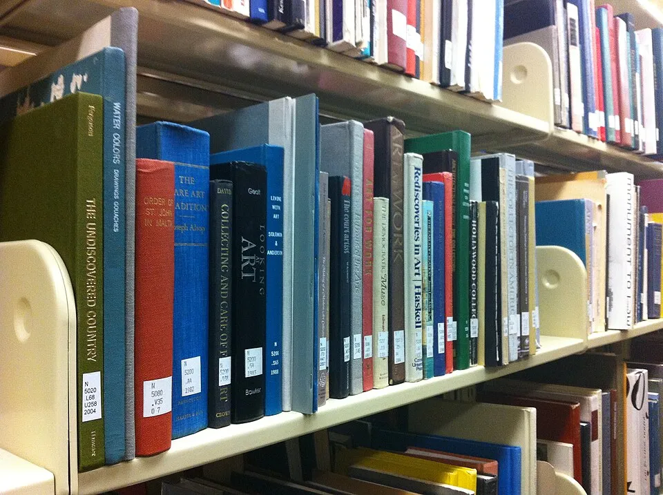 Art books arranged on a library shelf, the physical presence and visual weight that makes coffee table books different from other books, they are objects to display as much as to read