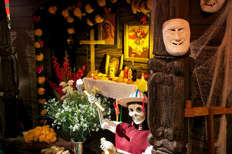 A colorful Día de los Muertos ofrenda altar with orange marigolds, candles, photographs, food offerings, and decorative skulls, demonstrating the Mexican celebration of death with color