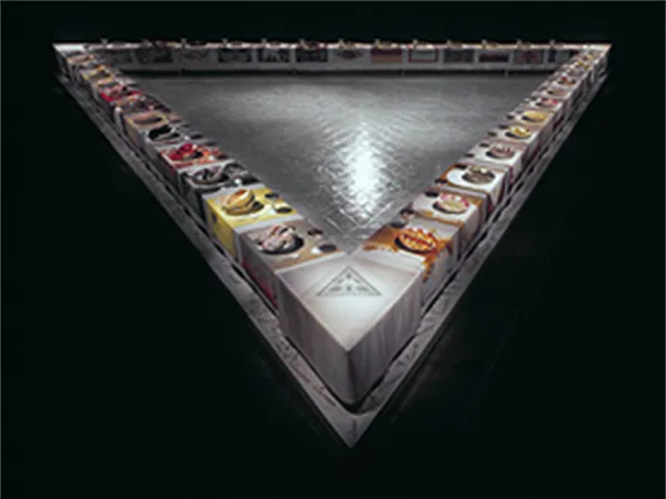 Judy Chicago, The Dinner Party (1974-1979). A large triangular banquet table with 39 place settings, each with an embroidered runner and a ceramic plate featuring butterfly/vaginal imagery, set on a floor inscribed with 999 names
