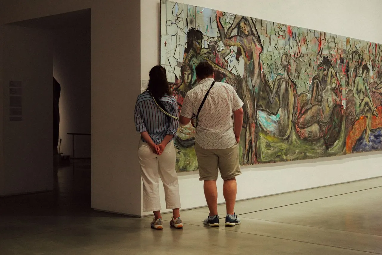 Two people in a gallery looking at a painting from different angles, demonstrating engaged looking