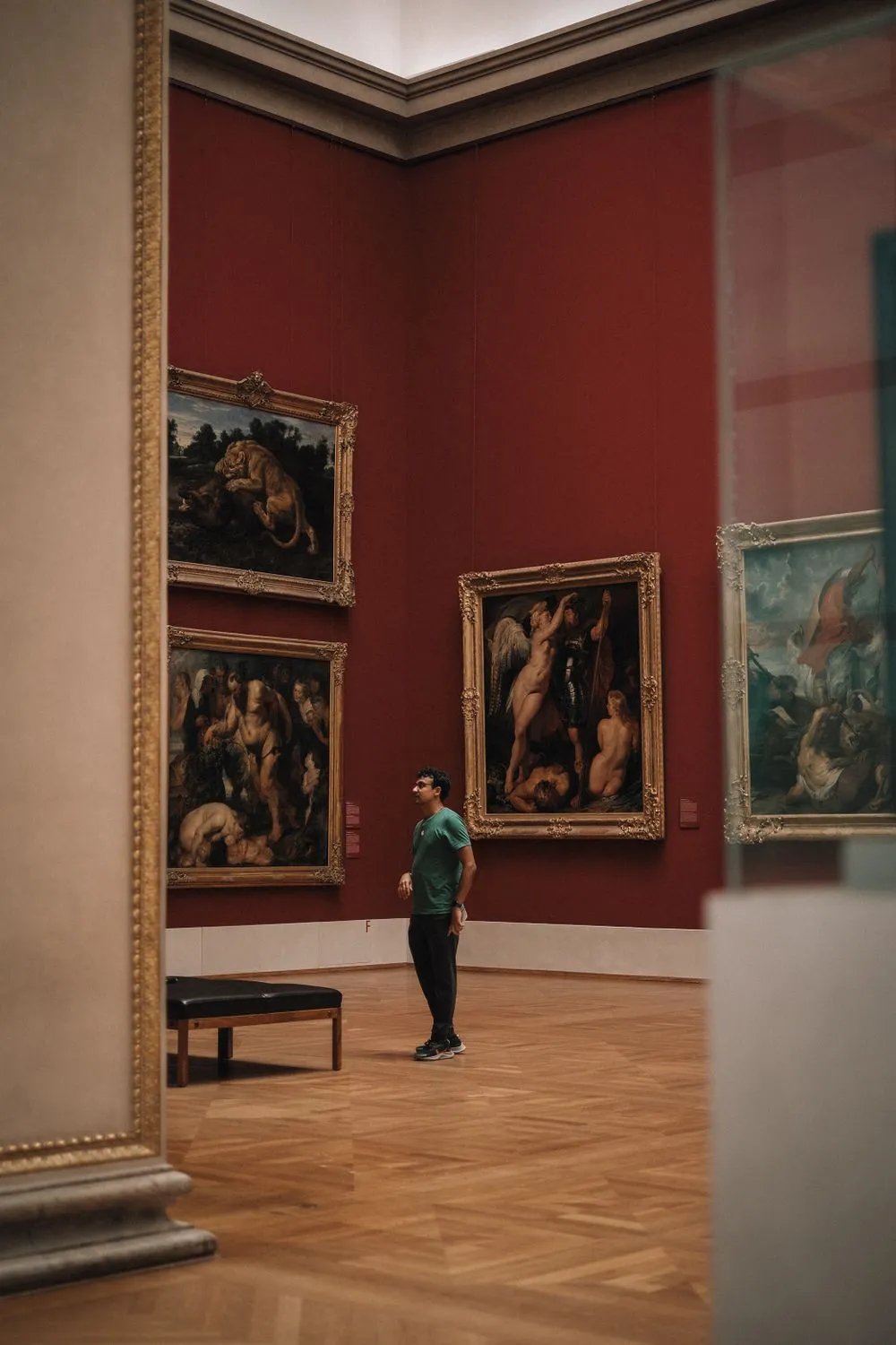 A man standing alone in a museum gallery, looking thoughtfully at paintings on the wall