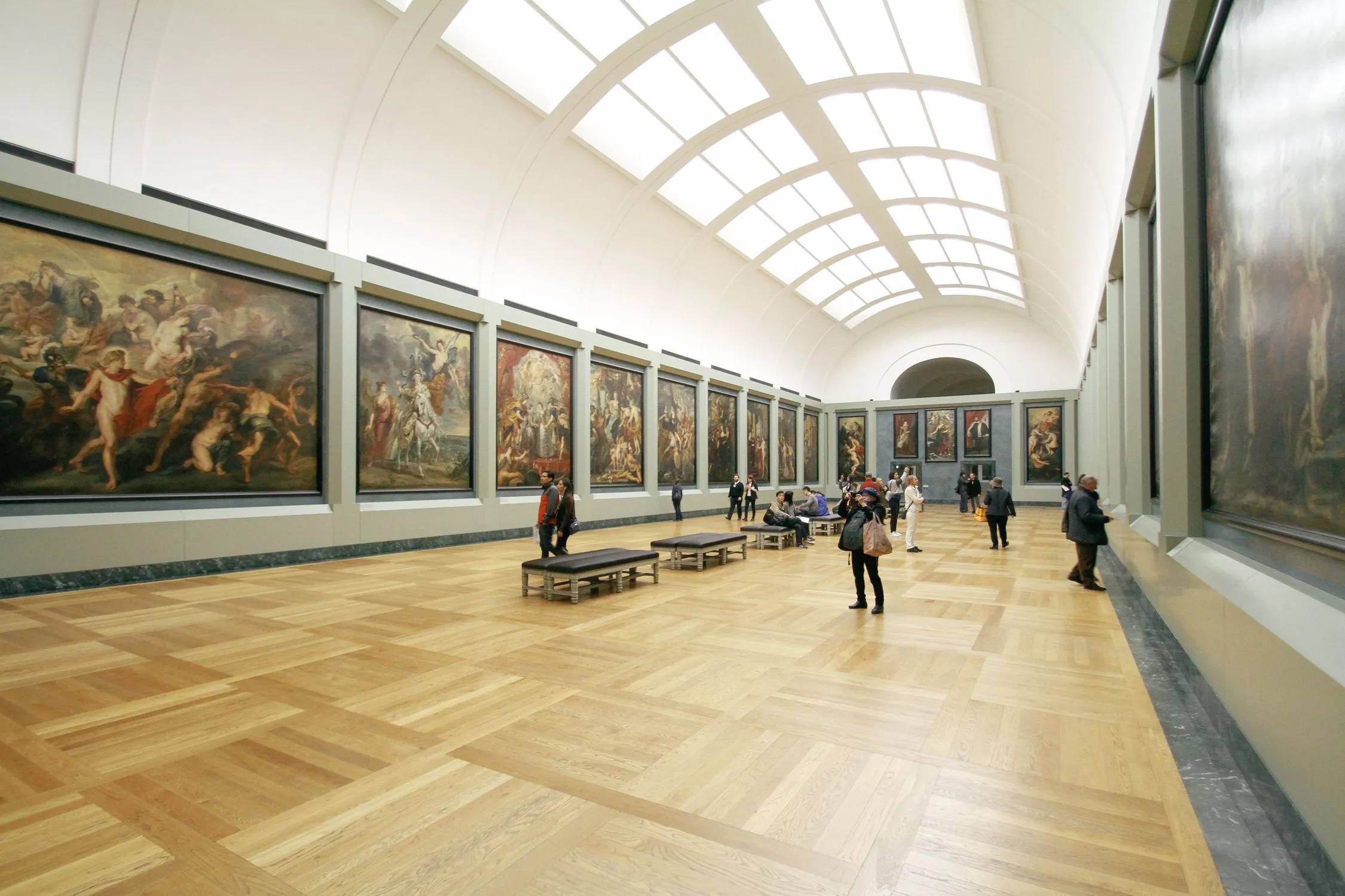 Interior of a grand art museum gallery with arched ceilings and paintings displayed on the walls, visitors walking through