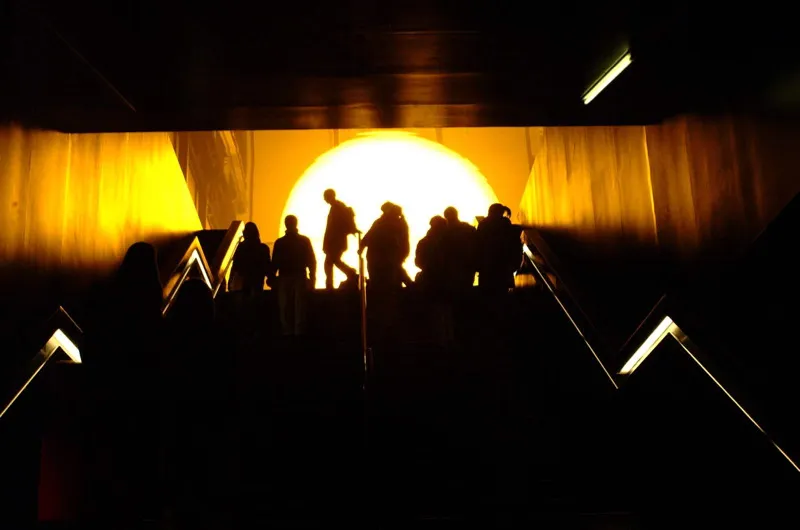 The Weather Project by Olafur Eliasson in the Turbine Hall of the Tate Modern, showing a large glowing artificial sun and visitors lying on the floor