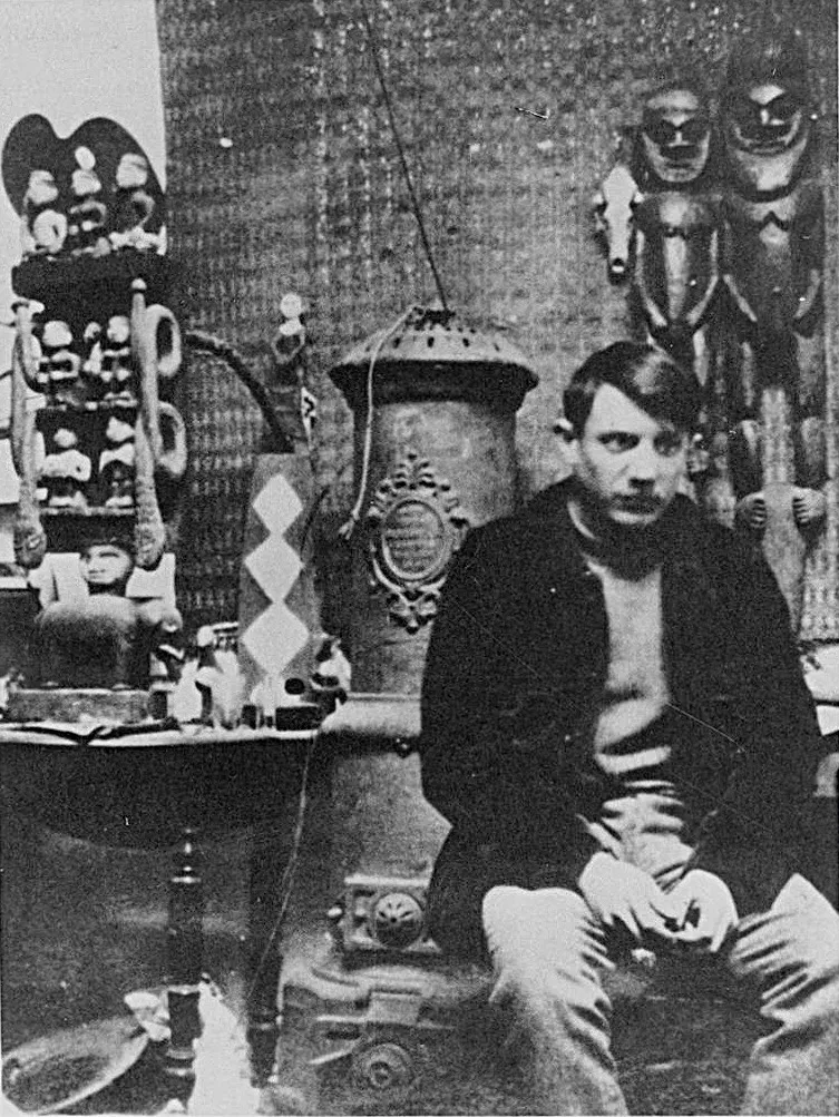 Pablo Picasso photographed in his studio in 1908, surrounded by his Cubist paintings and African masks that influenced his formal experiments