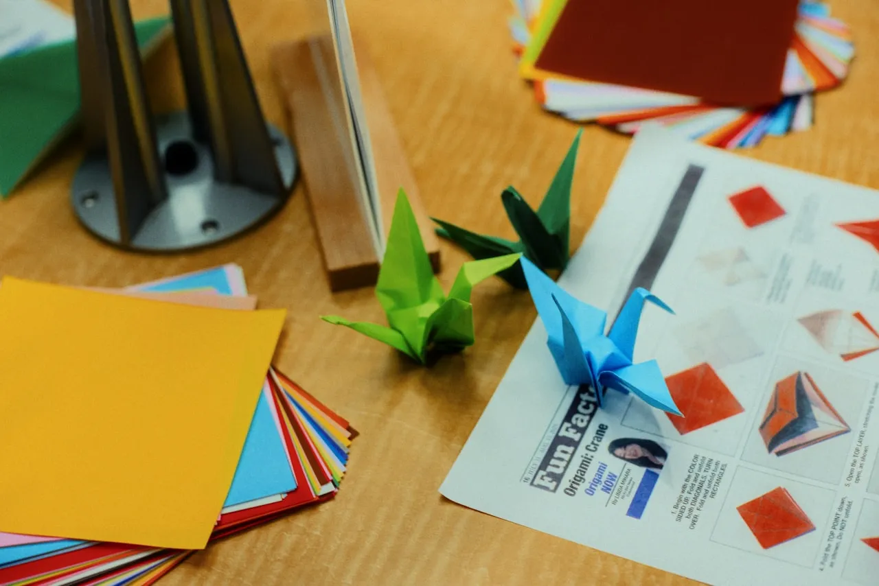 Origami cranes folded from coloured paper arranged on a flat surface, showing the completed three-dimensional forms and the folded paper material