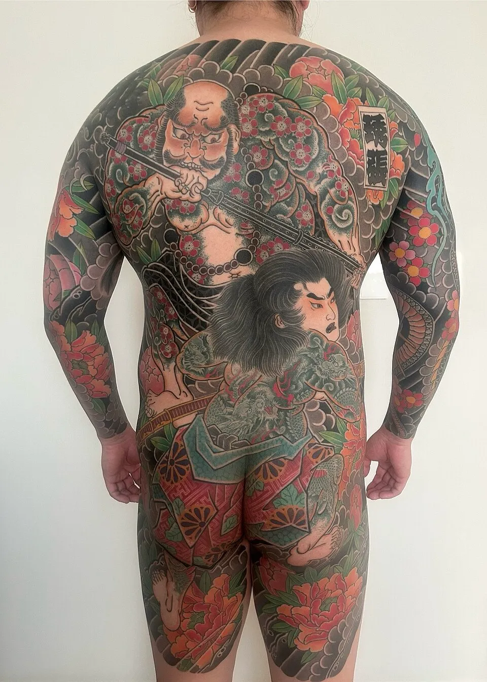 A Japanese woodblock print showing a figure with elaborate irezumi tattoos covering the body with mythological and natural motifs, dragons, koi fish, cherry blossoms, and waves, demonstrating the Japanese tattoo tradition