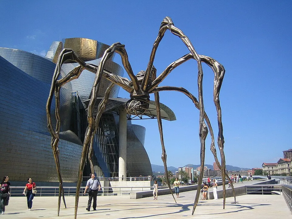 Louise Bourgeois, Maman, outside the Guggenheim Bilbao. A 9-meter tall bronze spider with a sac containing marble eggs, standing on long legs with the museum building visible behind.