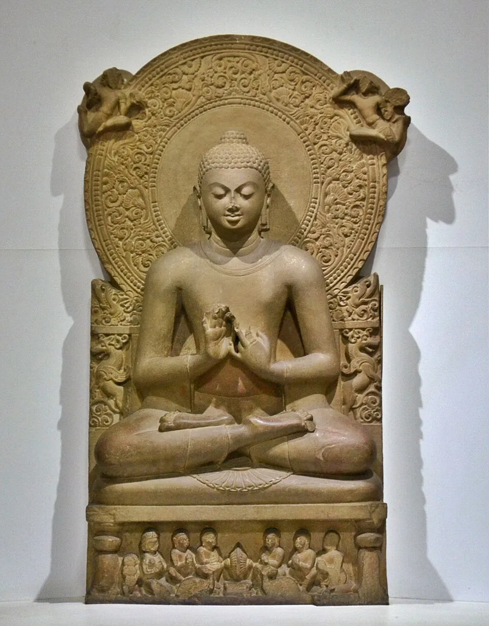 A Buddha statue showing the dharmachakra mudra, the gesture of turning the wheel of dharma, with both hands held at chest level, thumbs and index fingers forming circles, representing the teaching of the Buddha's first sermon