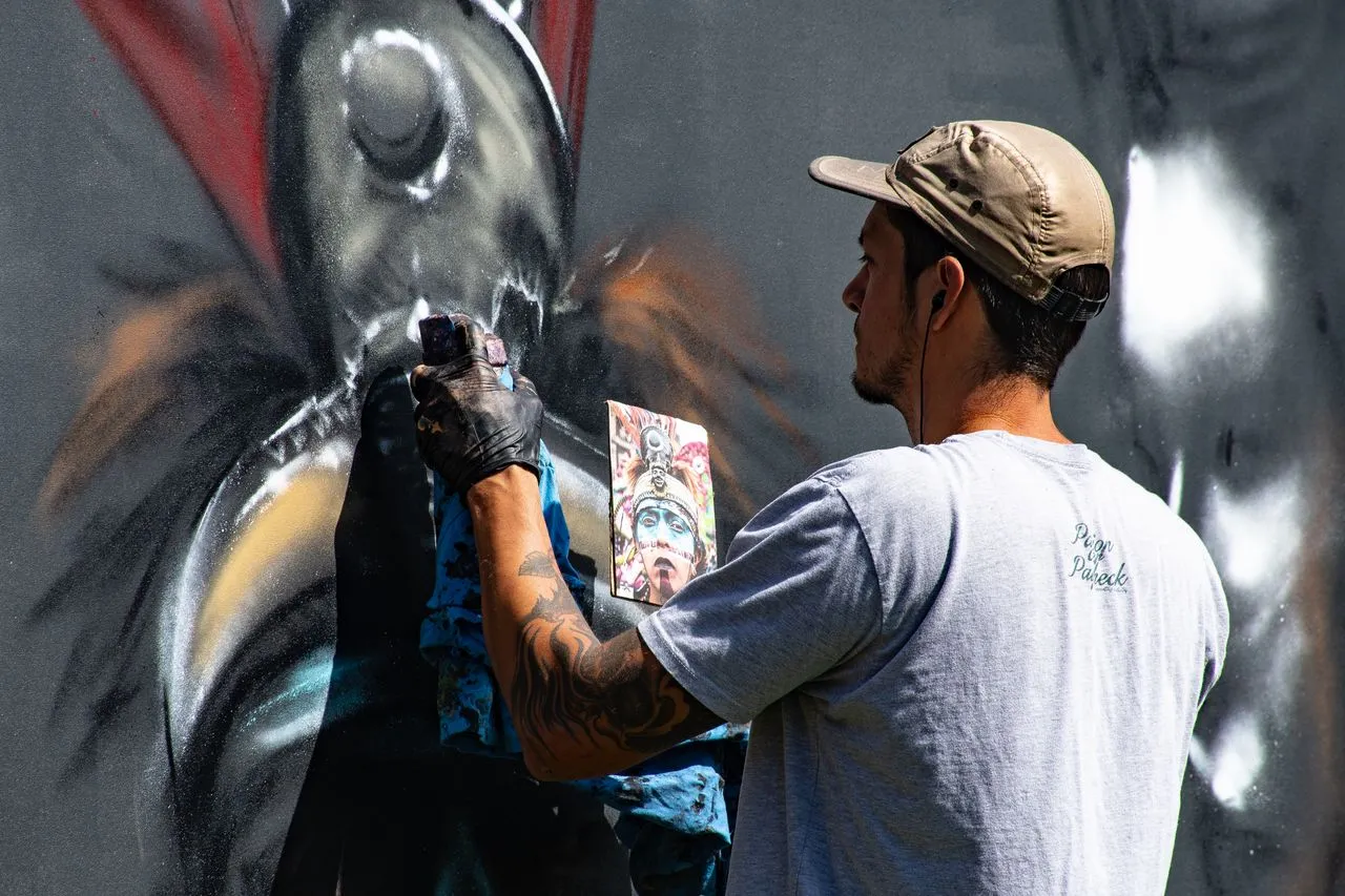 A man in a gray shirt spray painting art on a public wall, demonstrating that message and meaning can matter more than traditional technical refinement