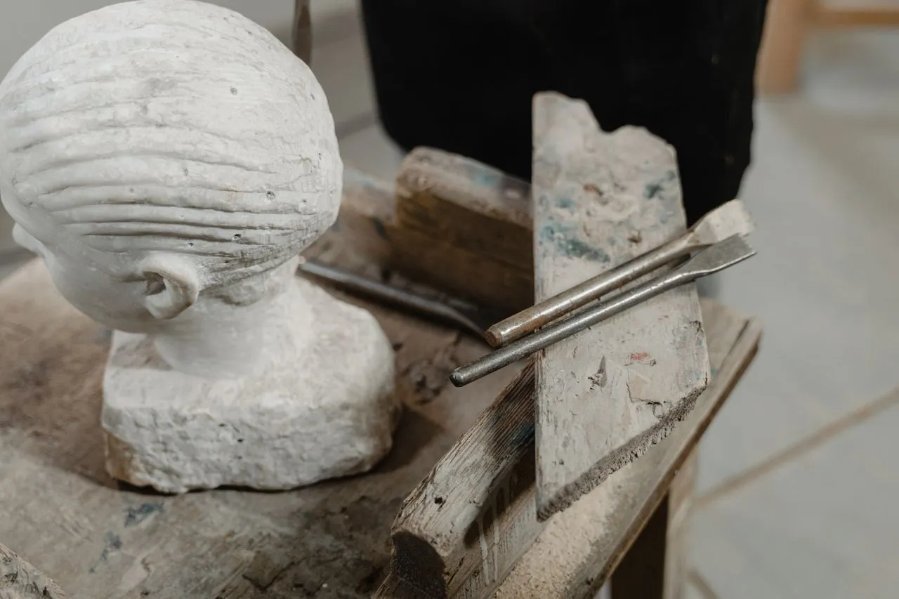 A head sculpture and sculpting tools on a wooden table, showing chisel marks that demonstrate mastery of craft and material control