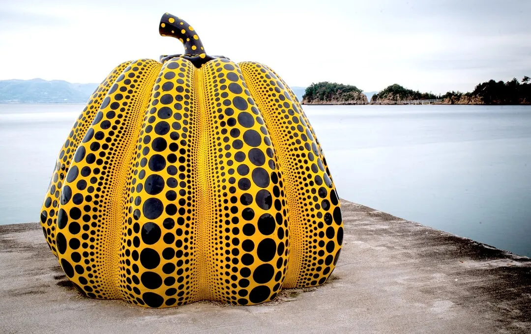 A large yellow pumpkin sculpture with black polka dots by Yayoi Kusama on the shore of Naoshima island, Japan